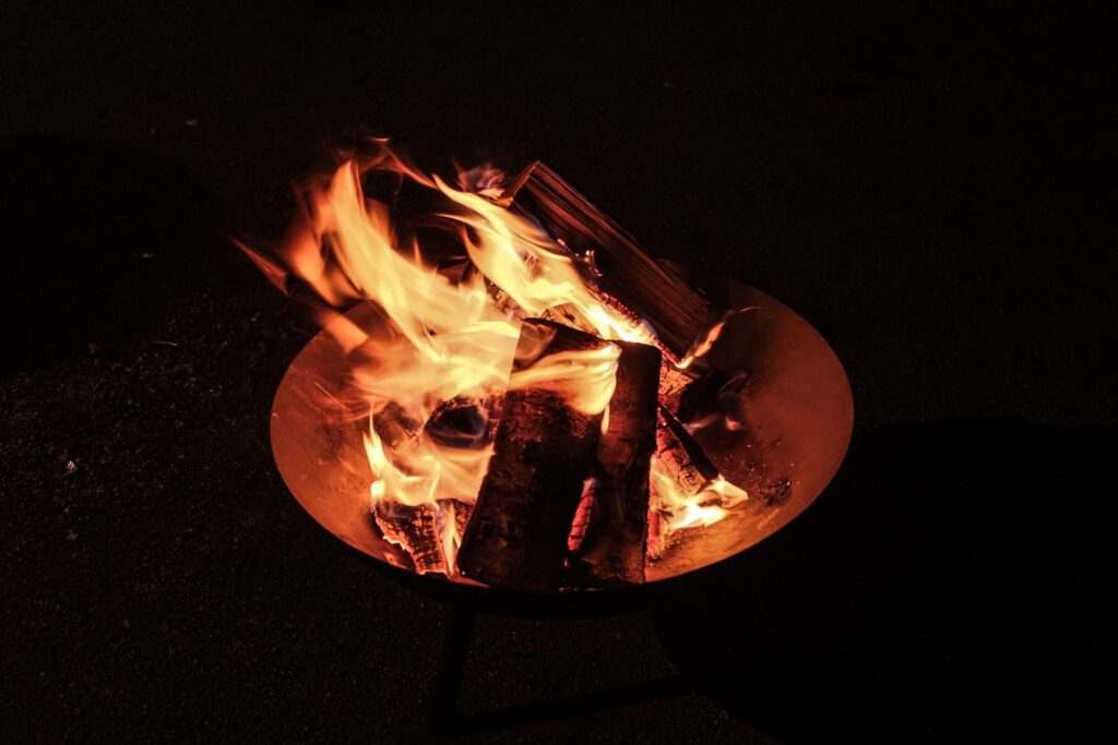 Open fire pit bowl with burning logs at night — compared against a clay chiminea