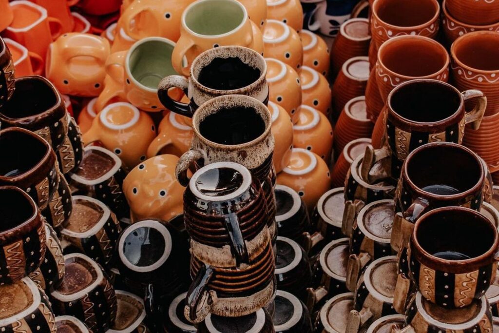 Colorful handmade glazed ceramic mugs stacked at a pottery market — gift ideas